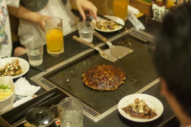 personas comiendo okonomiyaki placa hierro